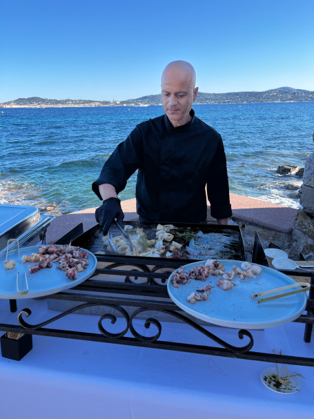 Chef préparant des plats de fruits de mer en bord de mer, avec des assiettes à côté.