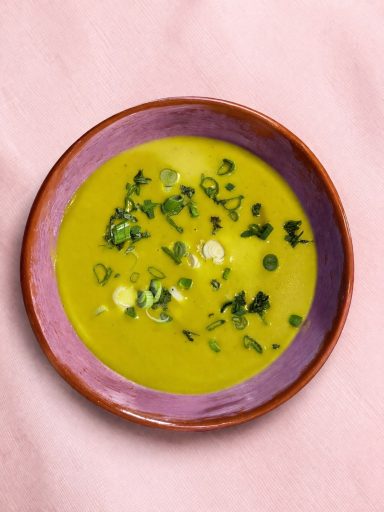 Soupe secrète du chef Soupe verte garnie d'oignons verts, servie dans un bol coloré sur fond rose.