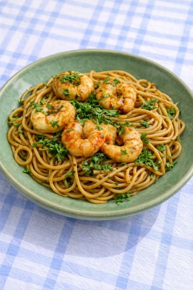 Des pâtes avec des crevettes et des herbes fraîches dans un bol vert.