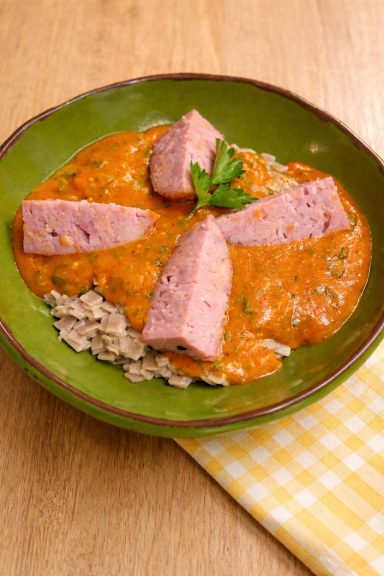 Plat de sauce rouge crémeuse avec morceaux de viande sur un lit de céréales.