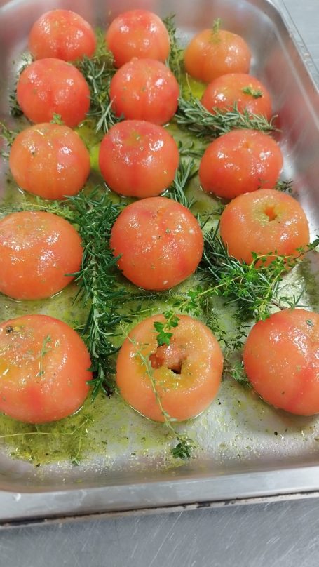Tomates mûres entourées d'herbes sur une plaque de cuisson.